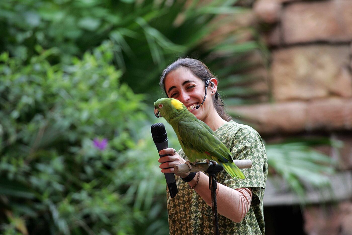 Cassie Malina, expert parrot trainer, with a green Amazon parrot perched calmly on her hand